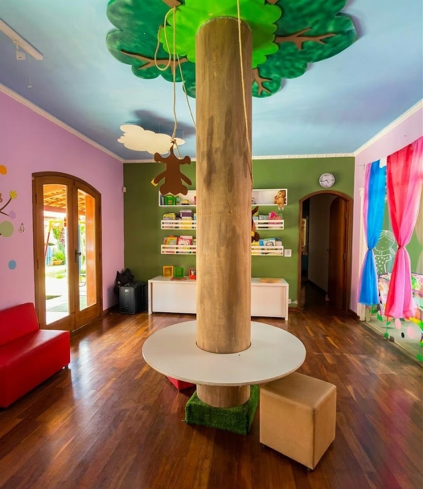 Espaço interno do Colégio Pingo de Gente com árvore cenográfica e ambiente de leitura