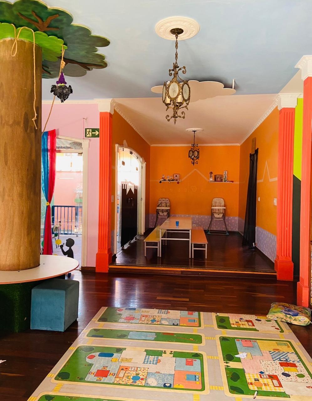 Sala colorida com tapete educativo e ambientes de brincadeira